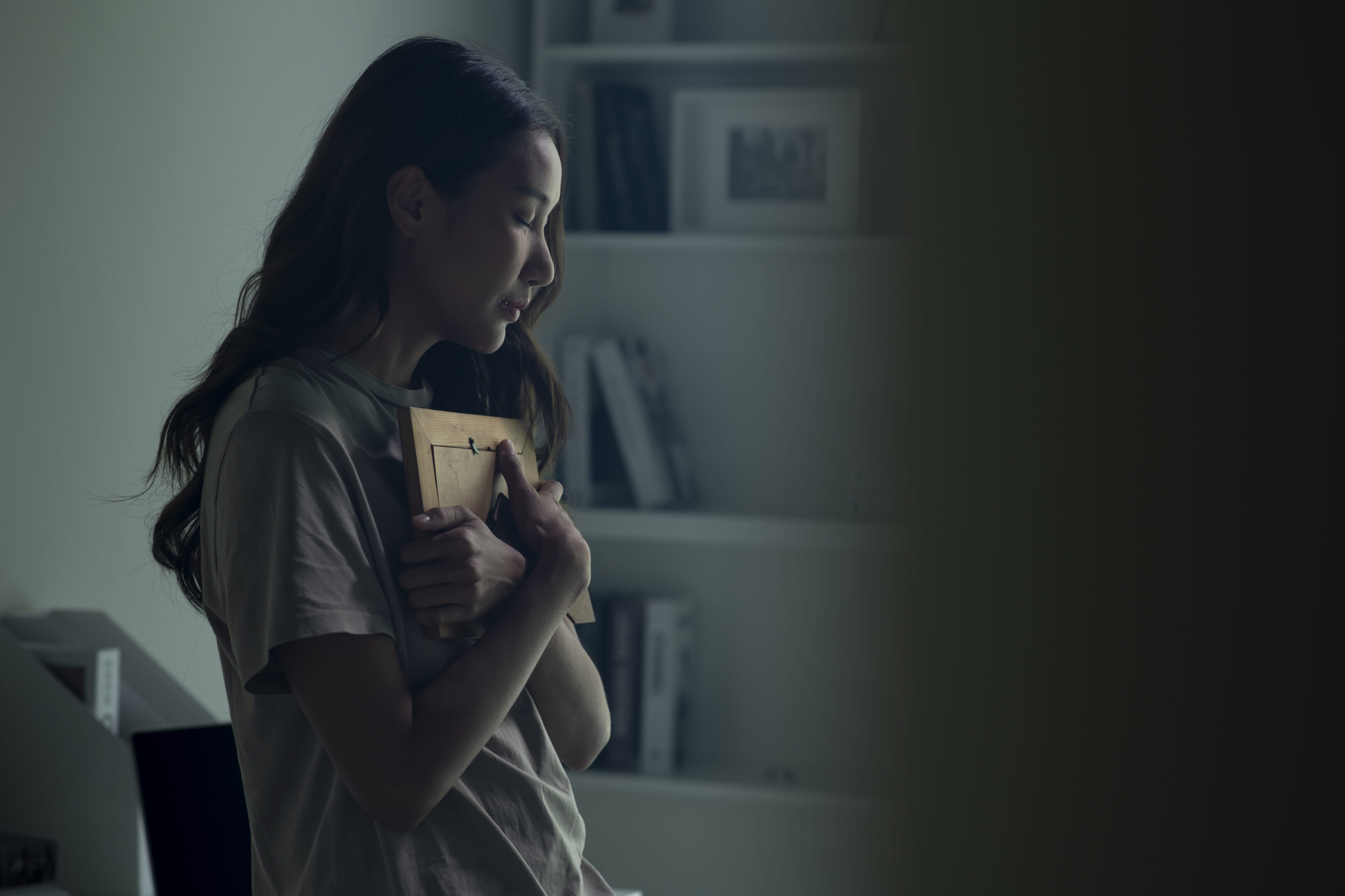 Asian women holding a photo frame of lost loved one and crying. Woman feeling sad when looking at picture of lost loved one in the frame. Depressed Asian women holding a photo frame of lost loved one and crying.